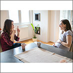 Women seated at table conversing in sign. One is pregnant and holding her stomach.