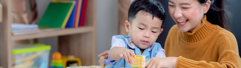 Mother smiling as her young child interacts with building blocks stamped with alphabet letters.