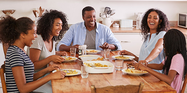 Parents and their three children sitting at their kitchen table, eating a meal together.