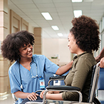 Medical professional with stethoscope attends to pregnant person in wheelchair.