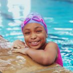 Child in swimming pool, head, neck and arms above water, poised at pool side ledge.