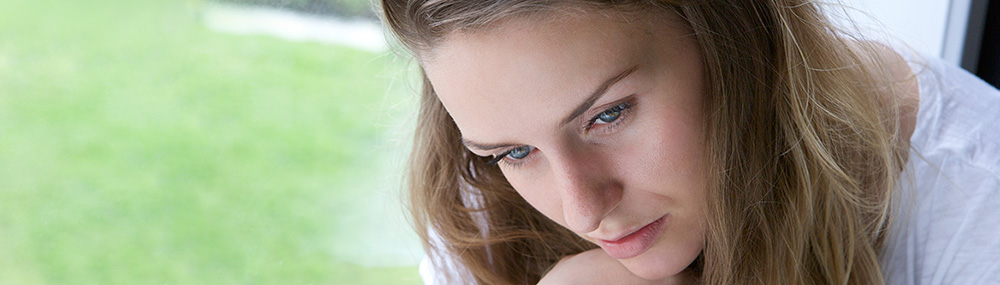 Woman looking down and sitting next to a window.