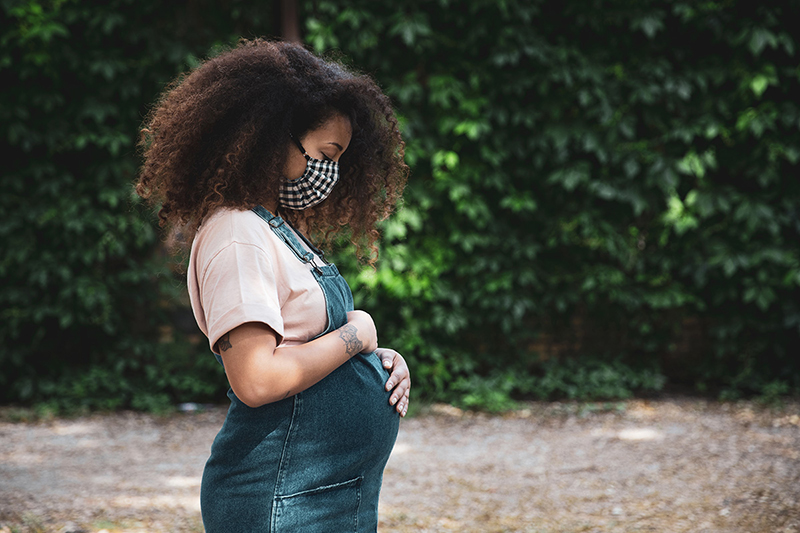 Pregnant woman outside wearing a mask.