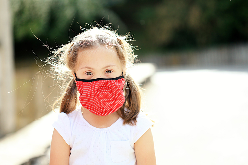 Child with down syndrome outside wearing a mask.