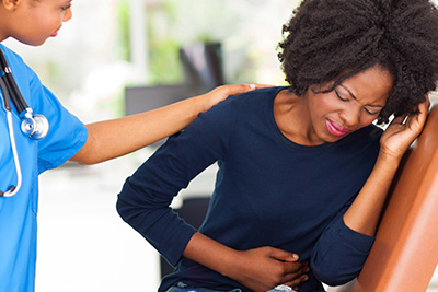 A woman holding her abdomen in pain while a doctor comforts her.