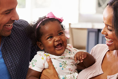 Two parents holding their infant between them and smiling. 