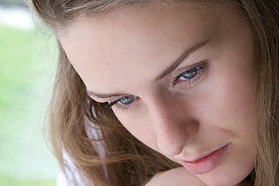 Woman looking down and sitting next to a window.